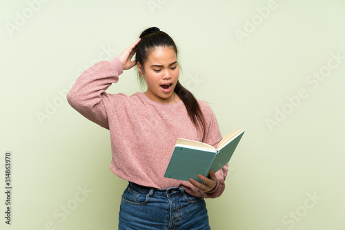 Young teenager Asian girl over isolated green background holding and reading a book