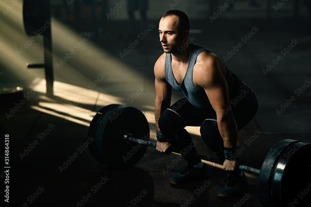 Muscular build man performing deadlift while having weight training in a gym.