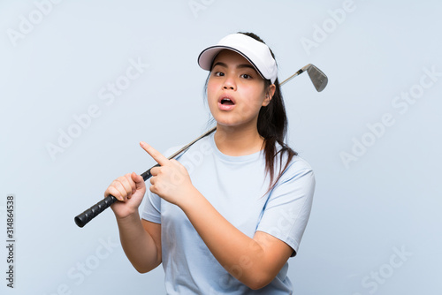 Young golfer Asian girl over isolated blue background surprised and pointing side