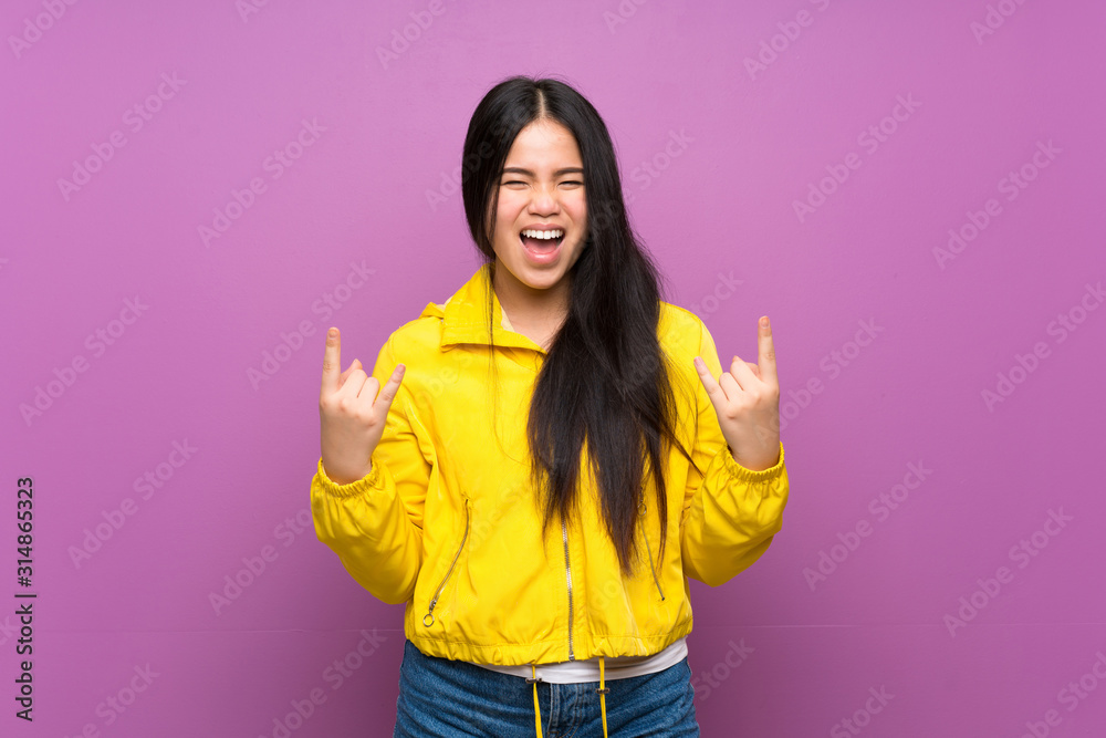 Young teenager Asian girl over isolated purple background making rock gesture Young teenager Asian girl over isolated purple background making rock gesture