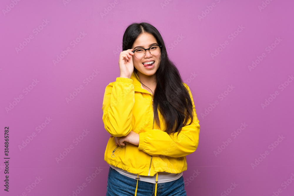 Young teenager Asian girl over isolated purple background with glasses and happy Young teenager Asian girl over isolated purple background with glasses and happy