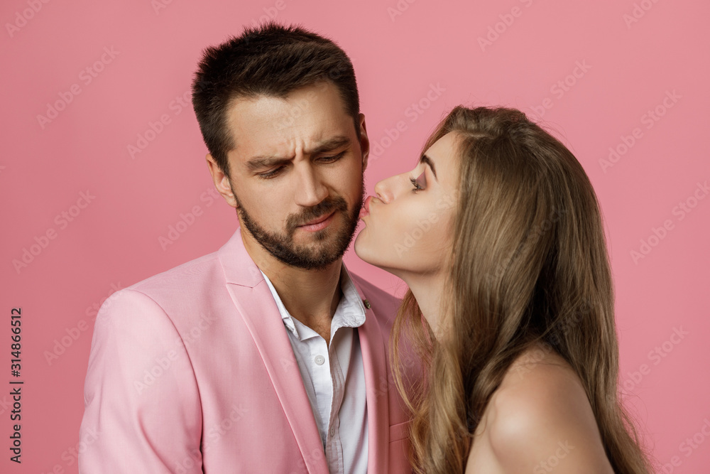 woman kissing her boyfriend. close-up. st valentines day. funny happy couple in love on pink background. woman kissing her boyfriend. close-up. st valentines day. funny happy couple in love on pink background.