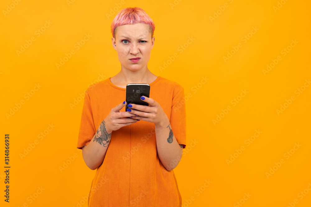 Extraordinary beautiful woman with short pink hair and big tattoo on her hand smiles isolated on orange background