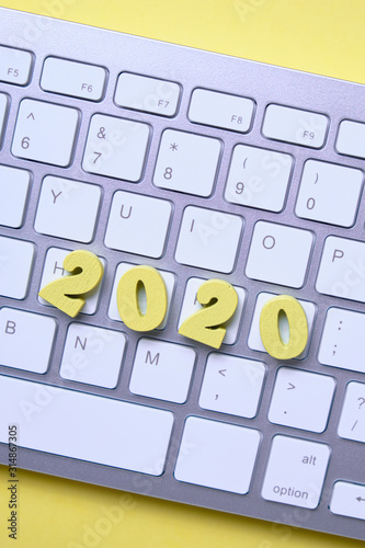 Wooden numbers 2020 on the keyboard on a yellow background. Top view.