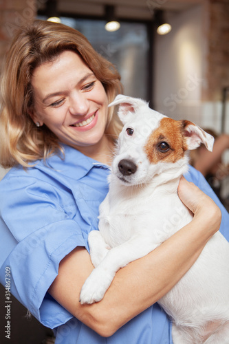 Vertical portrait of a happy mature female veterinarian hugging adorable jack russel terrier puppy. Healthy pets, medical care concept