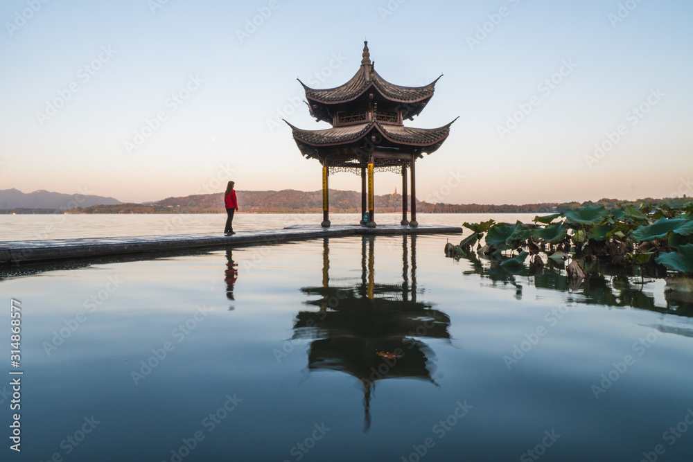 Sunrise panoramic view of the West Lake in Hangzhou, China. Girl silhouette in sunrise colors. Sunrise panoramic view of the West Lake in Hangzhou, China. Girl silhouette in sunrise colors.