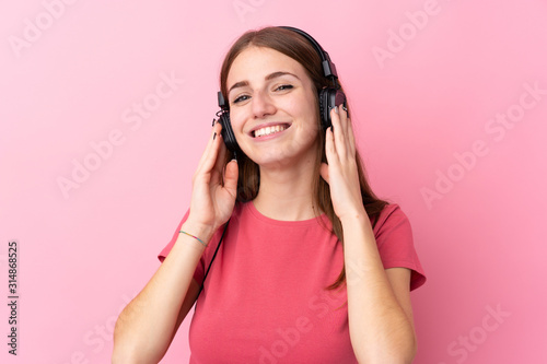 Young woman over isolated pink background listening music
