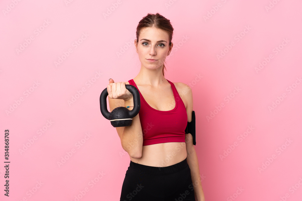 Young sport woman over isolated pink background making weightlifting with kettlebell and looking to the front