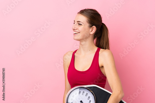 Young sport woman over isolated pink background with weighing machine