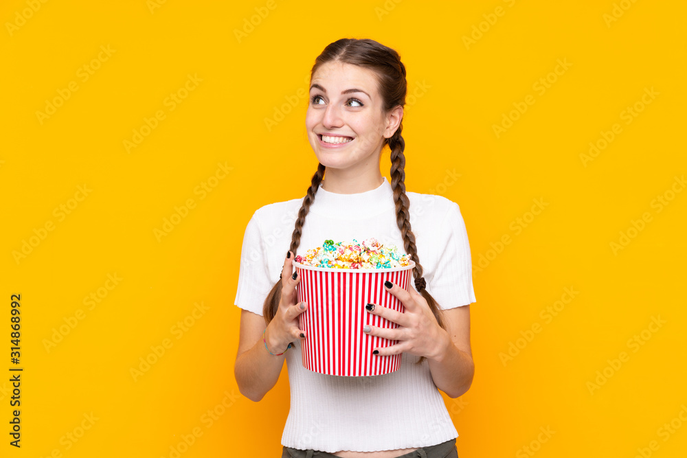 Young woman over isolated yellow background holding a big bucket of popcorns Young woman over isolated yellow background holding a big bucket of popcorns