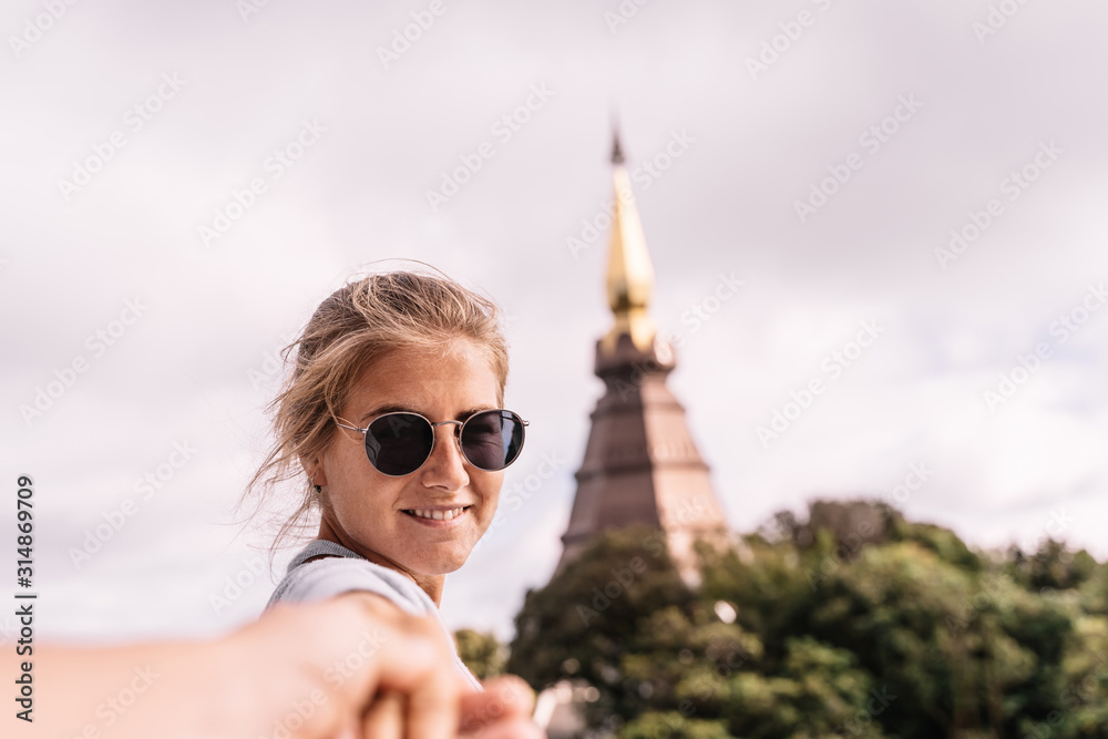 Blonde girl with sunglasses holding hands in front of a pagoda