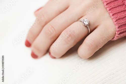 Close up of an elegant engagement diamond ring on woman finger with pink sweater winter clothe.