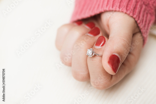 Close up of an elegant engagement diamond ring on woman finger with pink sweater winter clothe.