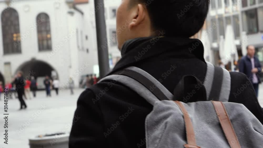 Young Asian man tourist traveling in city centre in Europe. Male backpacker walking in Marienplatz square, Munich, Germany. Traveling to Europe concept Young Asian man tourist traveling in city centre in Europe. Male backpacker walking in Marienplatz square, Munich, Germany. Traveling to Europe concept