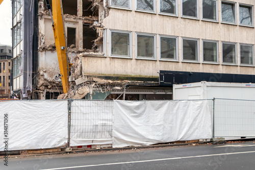 Abriss eines alten maroden Gebäudekomplexes per Abrissbagger schafft Platz für neue Architektur in urbanen Lebensräumen zur Stadtentwicklung nach Erdbeben mit Einsturzgefahr photo