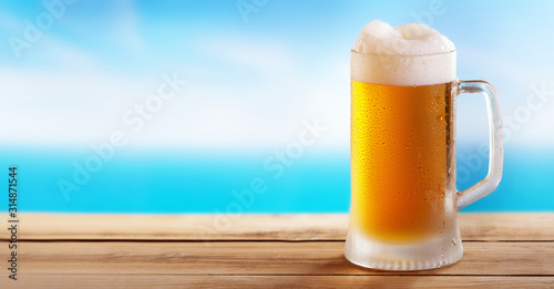 Canvas Print cold mug of beer on a wooden table on background of the sea