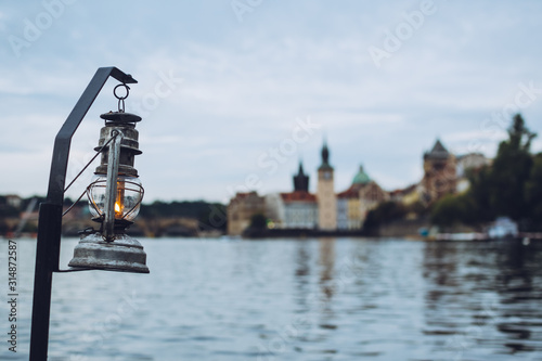 Old vintage lantern hanging over the waters of Vltava river in the beautiful city of Prague, one of the most popular European travel destinations. Admiring a romantic sunset from a boat.