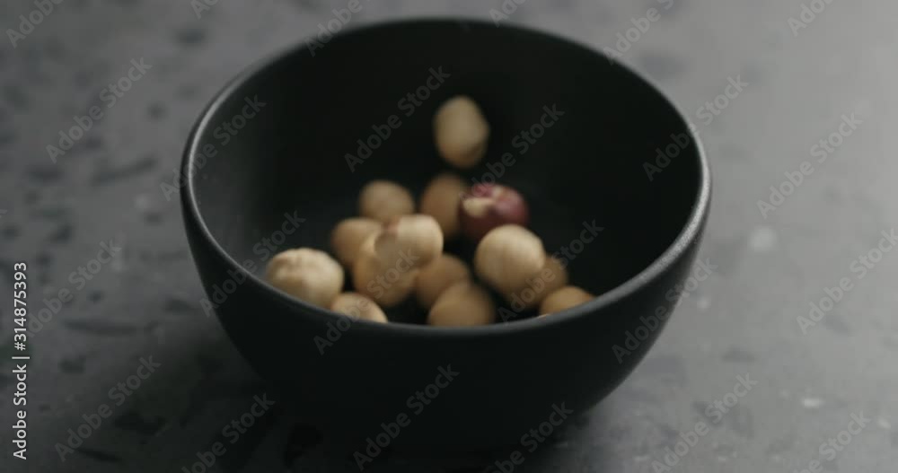 Slow motion roasted hazelnuts falling into black bowl on terrazzo countertop Slow motion roasted hazelnuts falling into black bowl on terrazzo countertop