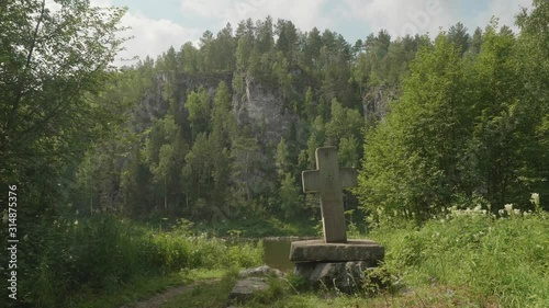 View of old cross as a symbol of birth of Demidov in 1779. View from floating raft on river bank covered with green thick forest. photo