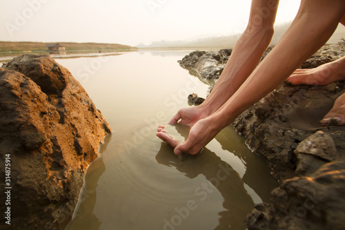 Fotografia Hand of Thirsty Man taking water from drying river on summer metaphor water crisis and climate change impact
