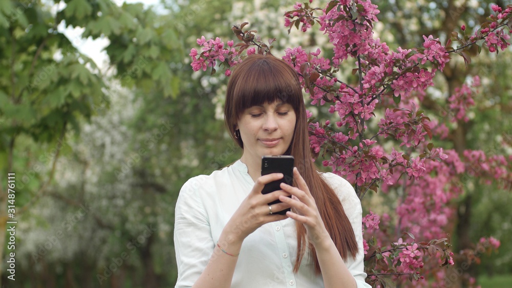 Girl makes selfie in the garden. An attractive red-haired woman smiles making selfi using a mobile phone in a cherry orchard. The concept of using gadgets for a healthy lifestyle. Girl makes selfie in the garden. An attractive red-haired woman smiles making selfi using a mobile phone in a cherry orchard. The concept of using gadgets for a healthy lifestyle.
