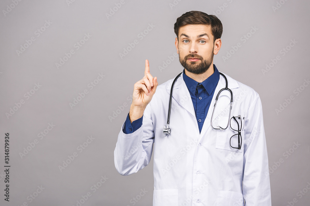 Portrait of cheerful smiling young doctor with stethoscope over neck in medical coat standing against isolated gray background. Portrait of cheerful smiling young doctor with stethoscope over neck in medical coat standing against isolated gray background.