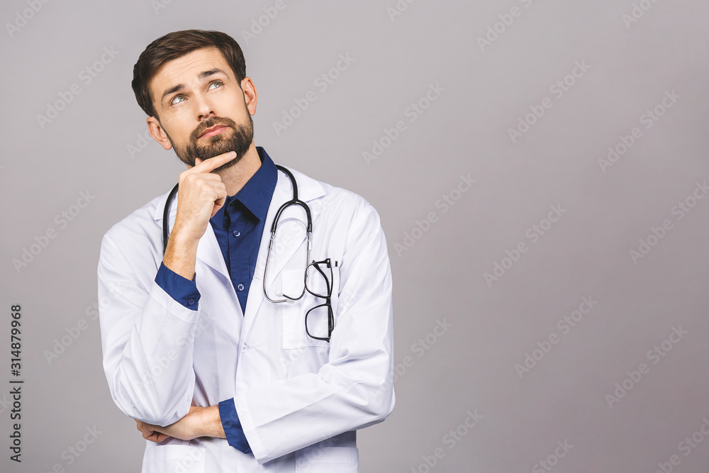 Portrait of serious young doctor with stethoscope over neck in medical coat standing against isolated gray background. Portrait of serious young doctor with stethoscope over neck in medical coat standing against isolated gray background.