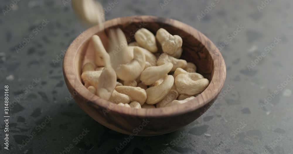 Slow motion dry cashew falling into olive bowl on terrazzo countertop Slow motion dry cashew falling into olive bowl on terrazzo countertop