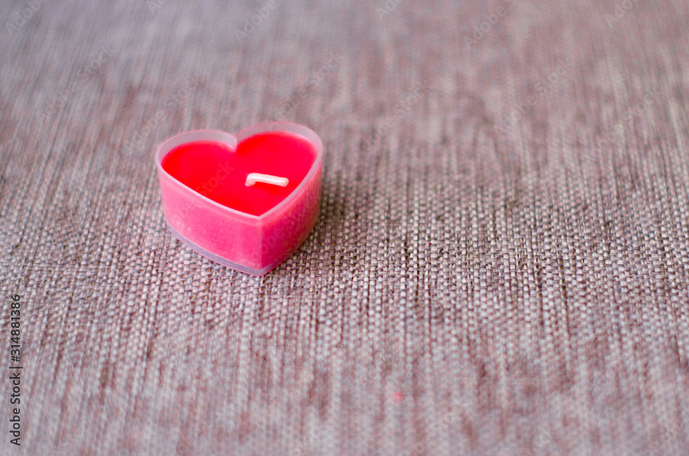Fototapeta premium One red candle in the shape of heart on the background of burlap. Close up. The view from the top. Valentine's day. Selective focus.