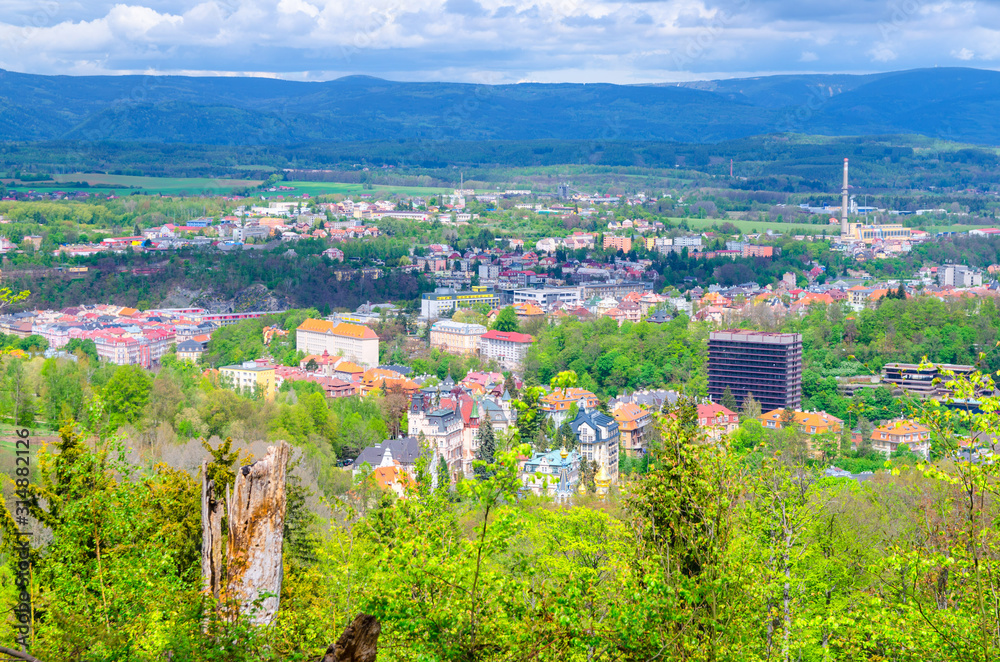 Top aerial panoramic view of Karlovy Vary (Carlsbad) spa town with colorful beautiful buildings, Slavkov Forest with green trees and Ore Mountain range background, West Bohemia, Czech Republic