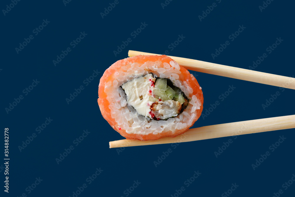 close up fresh salmon sushi roll with wooden chopsticks isolated on dark blue background. copy space. pantone color of year 2020. close up fresh salmon sushi roll with wooden chopsticks isolated on dark blue background. copy space. pantone color of year 2020.