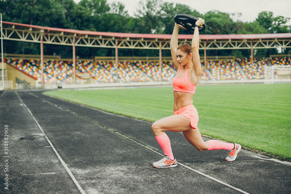 Sports girl at the stadium. Beautiful girl doing sports.The girl raises the weight