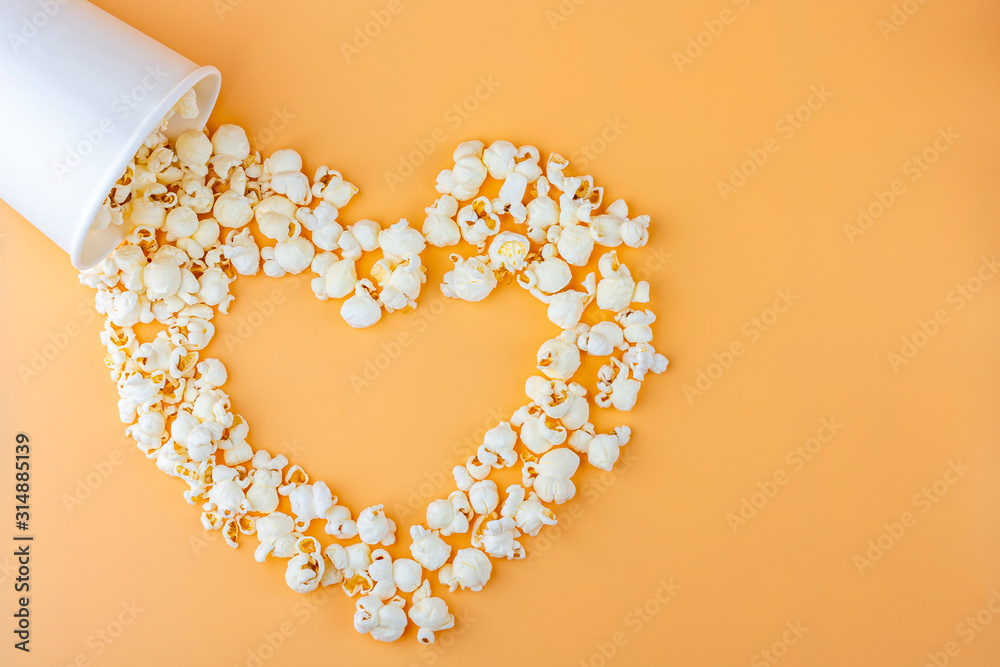 Love movies concept. Popcorn in paper box scattered on orange background heart shaped top view, copy space for text. Cinema snack concept. Popcorn box mocap