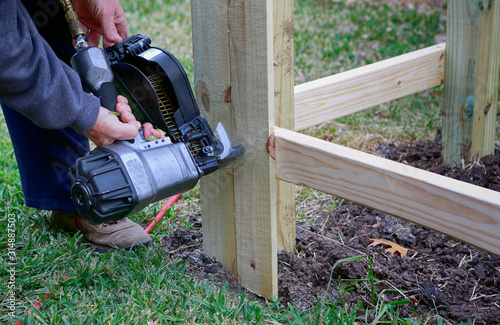 Building a new fence. Worker using a nail gun to attach wood pickets to the rail for new fence.