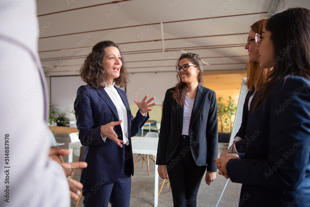 Smiling mature employee talking with younger colleagues. Cheerful office managers talking in office. Communication concept Smiling mature employee talking with younger colleagues. Cheerful office managers talking in office. Communication concept