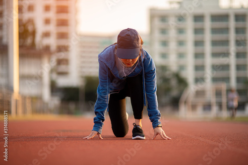 Athlete woman in running start pose on the city street. Sport tight clothes. Bright sunset, blurry background. Horizontal