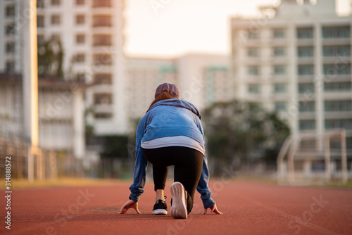 Athlete woman in running start pose on the city street. Sport tight clothes. Bright sunset, blurry background. Horizontal