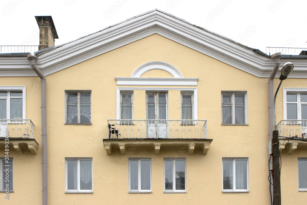 wide balcony of the old yellow building. Triangular roof, white frames, minimalism