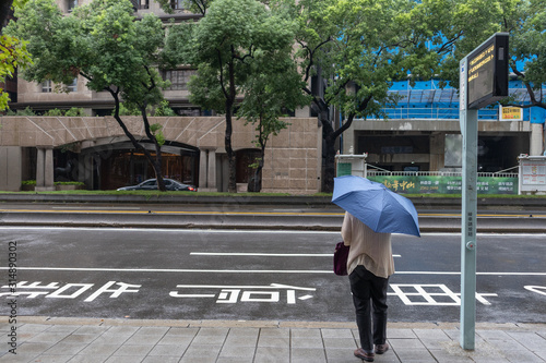 Taipei, Taiwan - SEP 14, 2019: Asian woman holding an umbrella in raining, waiting bus at bus stop in Taipei.