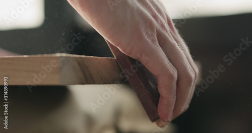 woodworker hand sanding walnut board with sand block