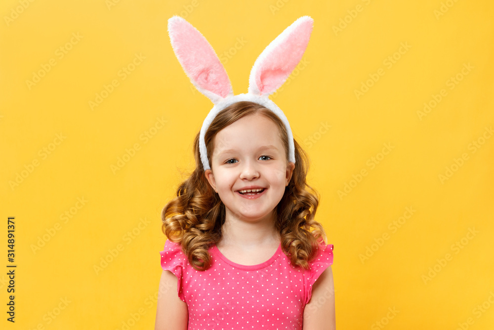 Happy cute little girl in easter bunny ears. Child close-up on a yellow background color