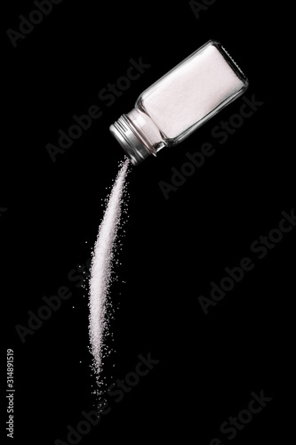 Salt is poured from a salt shaker on a black background. Salt shaker spills salt. A stream of salt. photo