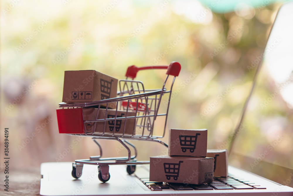 Shopping online concept - Parcel or Paper cartons with a shopping cart logo in a trolley on a laptop keyboard. Shopping service on The online web. offers home delivery...