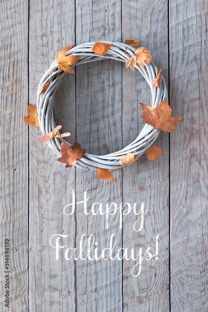 Wattle wreath with dry Autumn leaves on wooden background, greeting text 