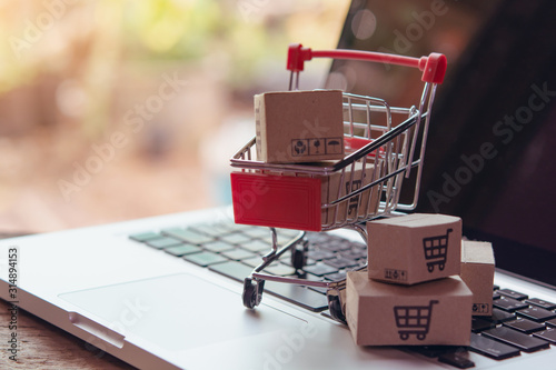 Shopping online concept - Parcel or Paper cartons with a shopping cart logo in a trolley on a laptop keyboard. Shopping service on The online web. offers home delivery... photo