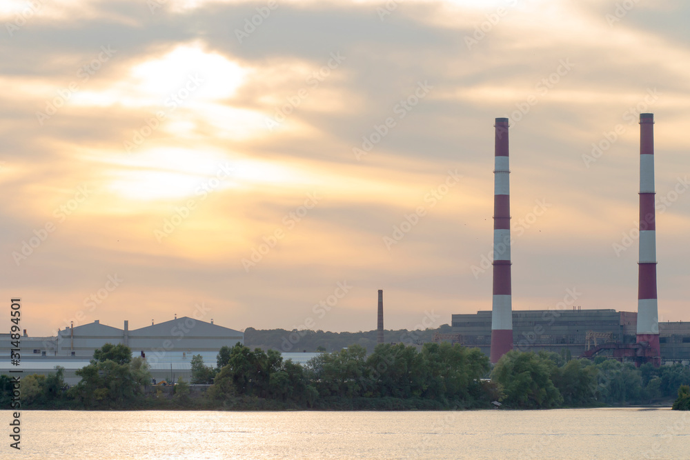 View of the shore in the greenery of plants with industrial towers at sunset
