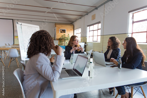 Group of professional businesswomen in meeting room. Multiethnic female colleagues sitting around table with laptops and discussing work in office. Women in business concept