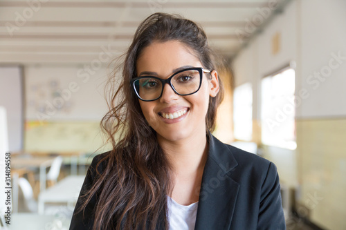 Cheerful young businesswoman smiling at camera. Portrait of attractive young businesswoman in eyeglasses smiling at camera in office. Business concept