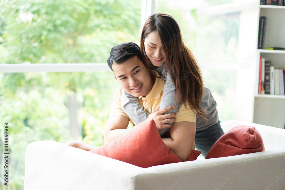 Happy couple sitting on the sofa and being a woman embracing her boyfriend with love in the living room and smile. Concept of romantic on valentine day. Proposal and marriage