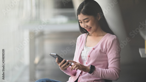 Smiling young beautiful girl while holding and looking at her phone. Happiness office worker concept.